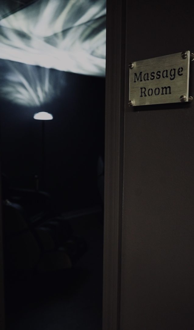 Massage Room door sign beside a dim room with a massage chair