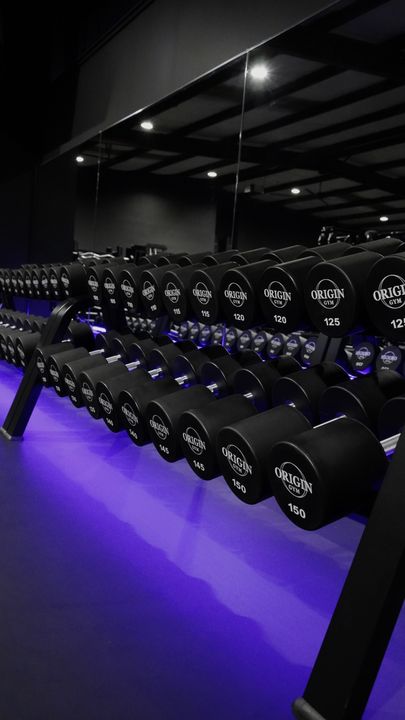 Origin branded dumbbell rack under violet floor lighting
