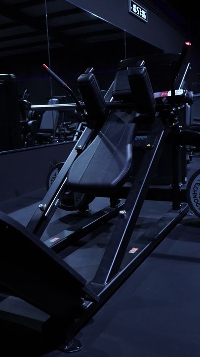 Angled leg press with black pads and the clock above