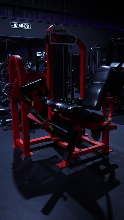 Red StriveFit leg extension machine beneath the floor clock