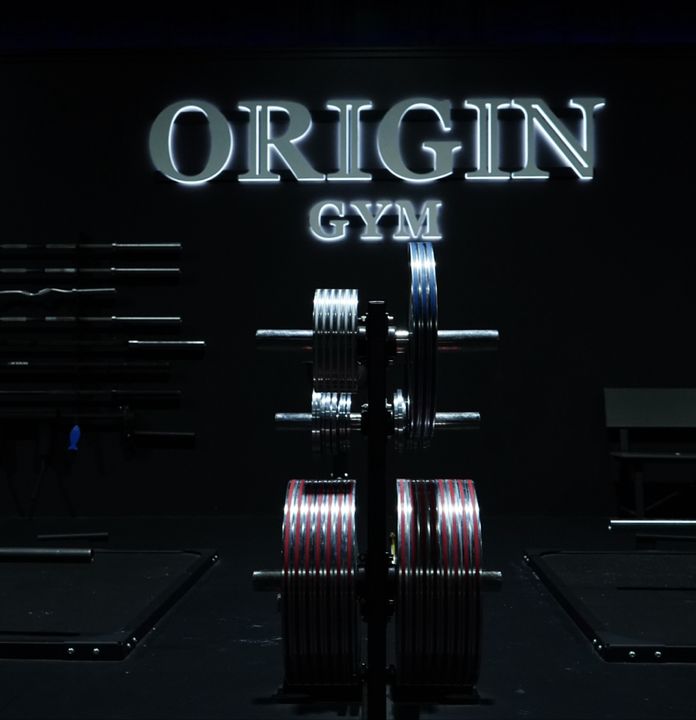 Lit ORIGIN GYM sign glowing above a loaded barbell